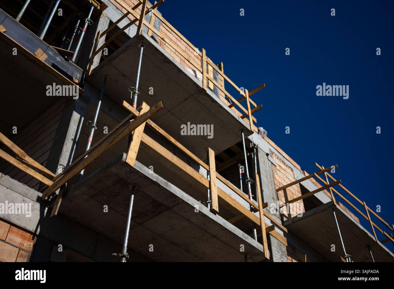 Stahlgerüst in einem neu errichteten Wohnblock aus rotem Backstein. Foto an einem sonnigen Tag mit blauem Himmel. Stockfoto