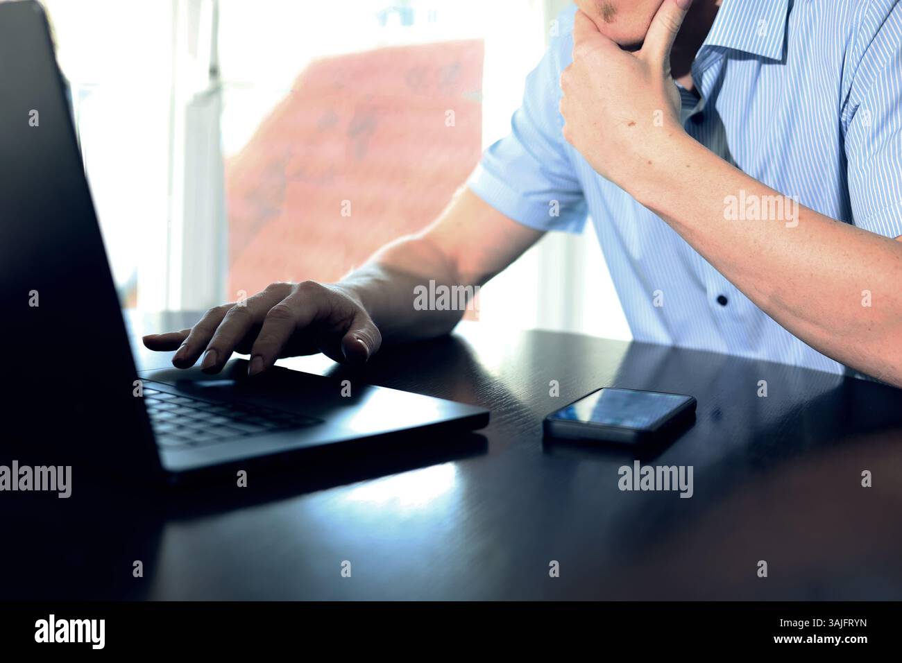 Geschäftsmann sitzt nachdenklich vor dem Laptop, Hand am Kinn Stockfoto