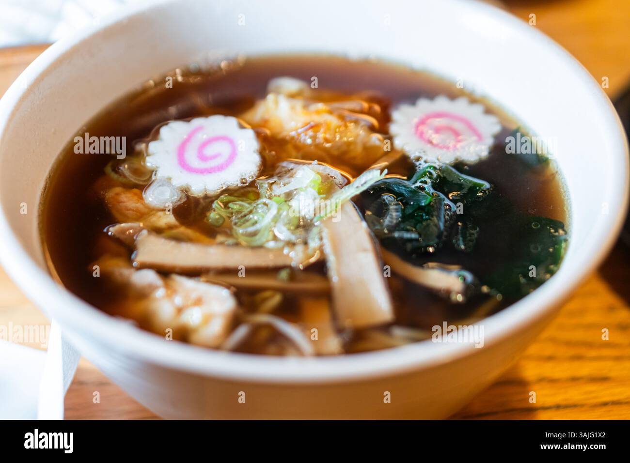 Eine Schüssel Ramen-Suppe mit verschiedenen Zutaten wie Nudeln, Algen, Fleischscheiben und dekorativen Fischkuchen. Die Brühe ist dunkel und geschmackvoll, gar Stockfoto