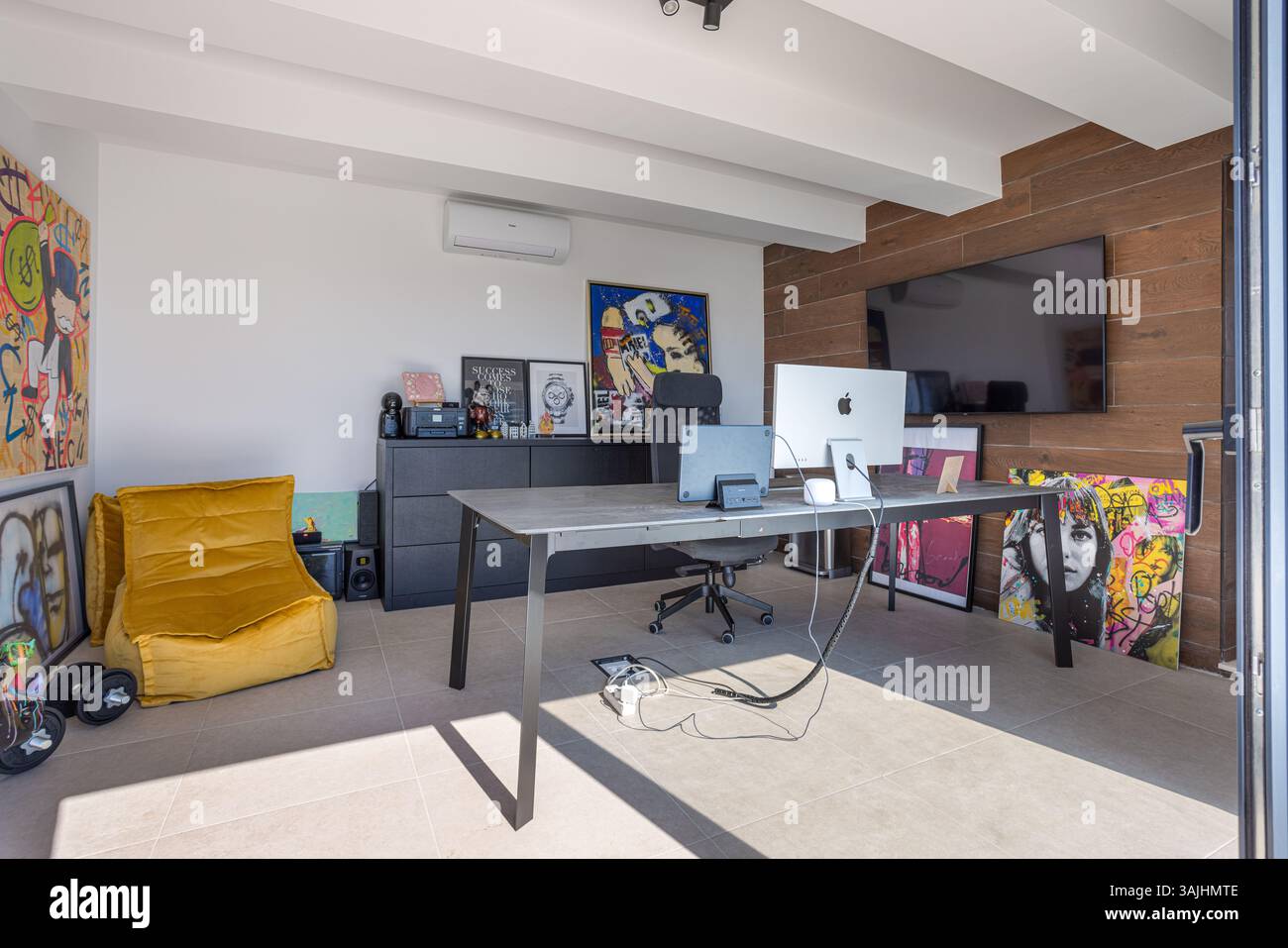Ein heller und künstlerischer Home Office-Bereich mit auffälliger Graffiti-Kunst, einem modernen schwarzen Schreibtisch und einem iMac-Setup mit Tageslicht. Stockfoto