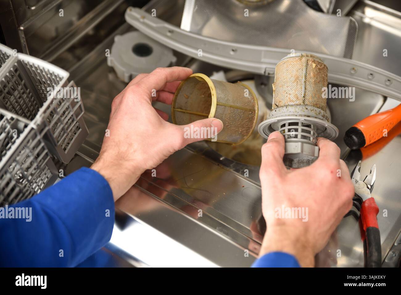 Detail der Hände eines Technikers mit schmutzigen Teilen eines Geschirrspülers, der Wartungsarbeiten mit Werkzeugen in der Nähe durchführt. Erhöhte Aussicht. Stockfoto