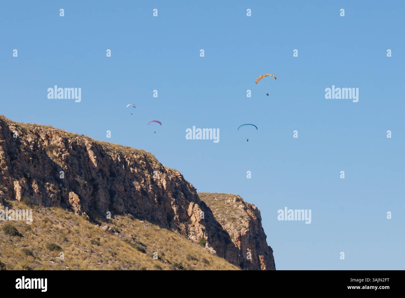 Gruppe von Gleitschirmfliegern, die gegen einen blauen Himmel über den Bergen fliegen, Alicante, Spanien Stockfoto