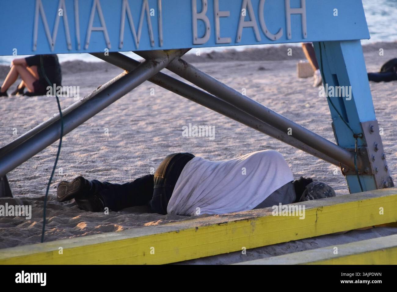 Die Person schläft rauh am Strand von Florida, umgeben von Sand und Meer, warmem Tageslicht, städtischer Armut, menschlichem Kampf, Reisedokumentarismus Stockfoto