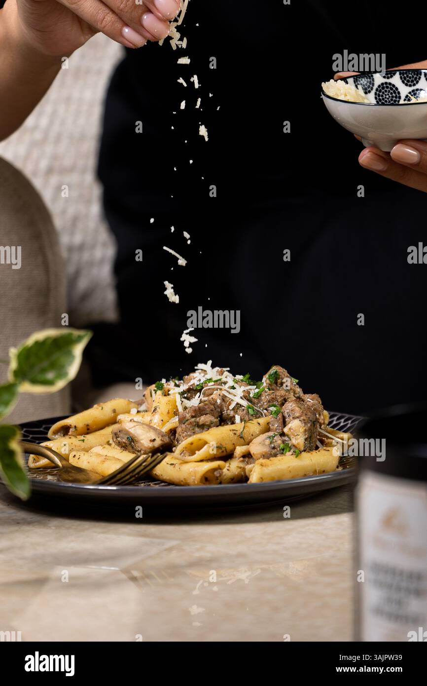 Cremige Pilznudeln mit extra Käse – Lifestyle-Aufnahme auf Beige Marmor mit grünen Blättern Stockfoto