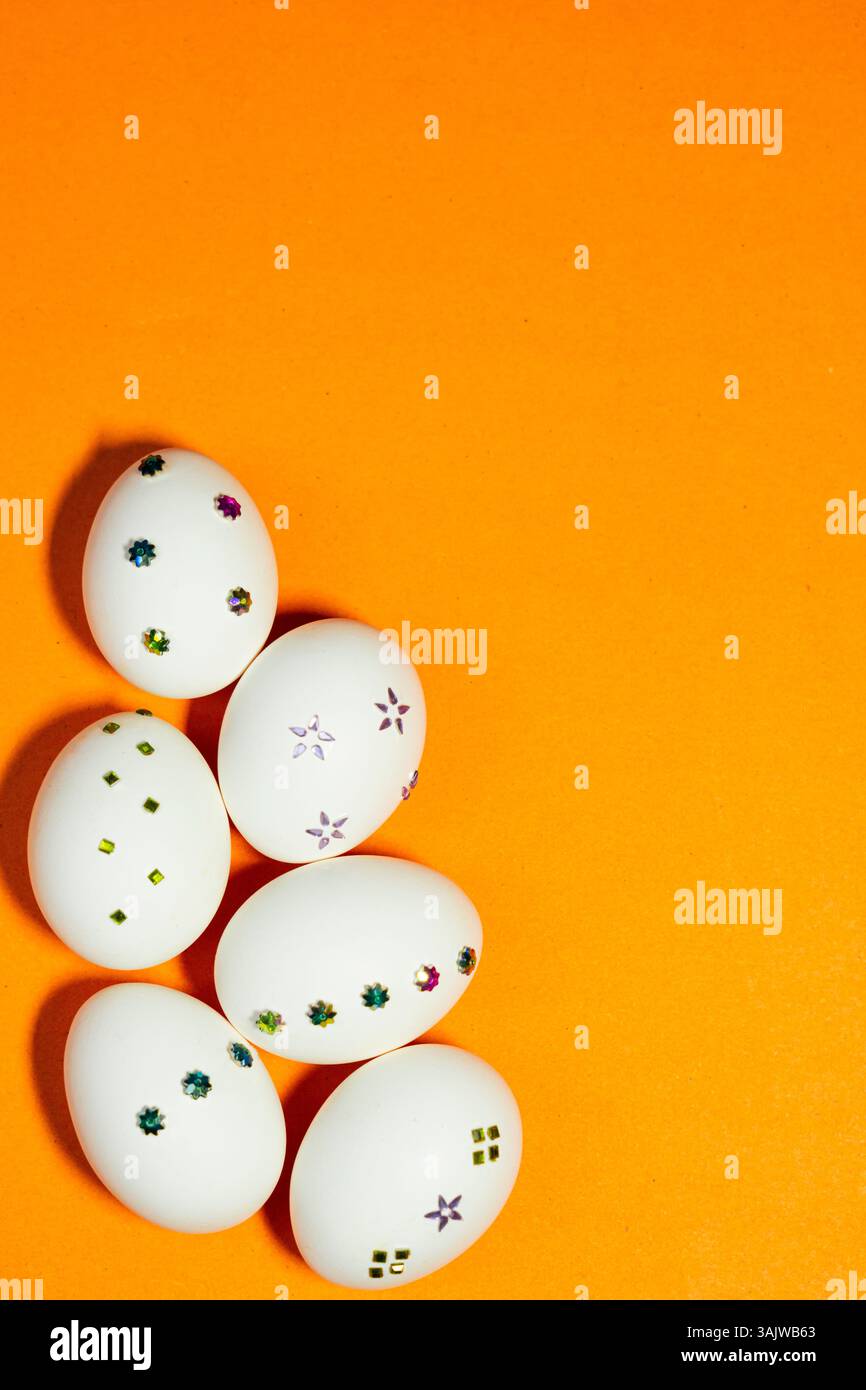 Minimalistisches Oster-Konzept mit weißen Eiern, die mit farbenfrohen Dekorationen verziert sind, und einem klaren, modernen, festlichen Look auf einem markanten orangefarbenen Hintergrund. Stockfoto