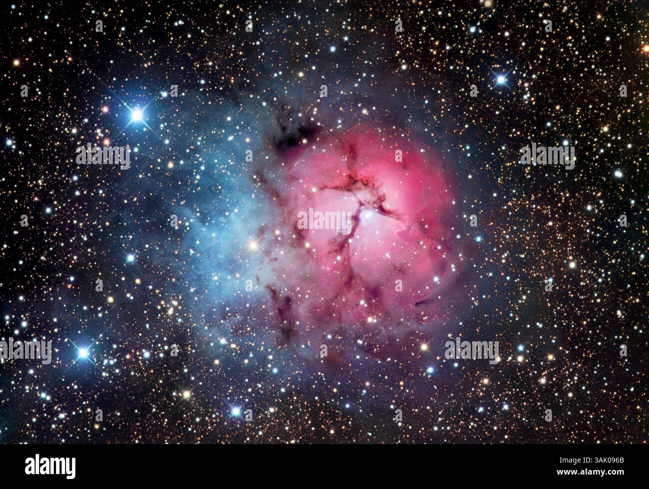 Trifidennebel (M20), optisches Bild. Dieser Nebel ist eine Region der Sternentstehung. Der rote Bereich ist ein Emissionsnebel, in dem die Strahlung heißer, neu gebildeter Sterne das umgebende Gas ionisiert und zum Leuchten bringt. Der blaue Bereich ist ein Reflexionsnebel, der kein Licht abgibt, sondern das Licht naher Sterne reflektiert. Reflexionsnebel erscheinen blau, weil kurzwelliges blaues Licht mehr als rot gestreut wird. Die dunklen Linien über dem Nebel werden durch dunkle Staubwolken im Vordergrund verursacht, die das Licht von hinten verdecken. Der Nebel liegt im Sternbild Sagittarius. Stockfoto