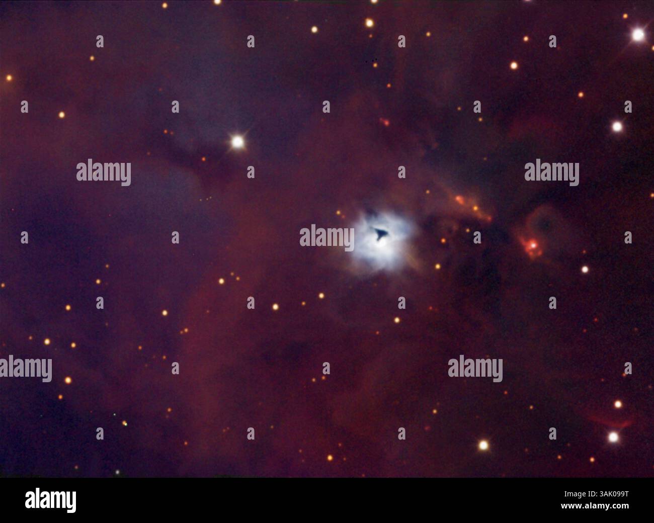 Reflexionsnebel NGC 1999 (weiß) mit einer Silhouettenglobule (schwarz). Die gesamte Region ist von einem schwachen Emissionsnebel (rot) umgeben. Reflexionsnebel strahlen kein eigenes Licht aus, sondern reflektieren das Licht naher Sterne. Da blaues Licht effektiver gestreut wird als rotes Licht, erscheinen sie in der Regel blau. Eine Bok Globule ist eine dichte Wolke aus Gas und Staub, die sich in fortgeschrittenen Stadien des Zusammenbruchs befindet und einen Stern oder Sterne bildet. Diese Nebel sind Teil des großen Orion-Komplexes, der zwischen 1500-1600 Lichtjahren von der Erde im Sternbild Orion liegt. Stockfoto