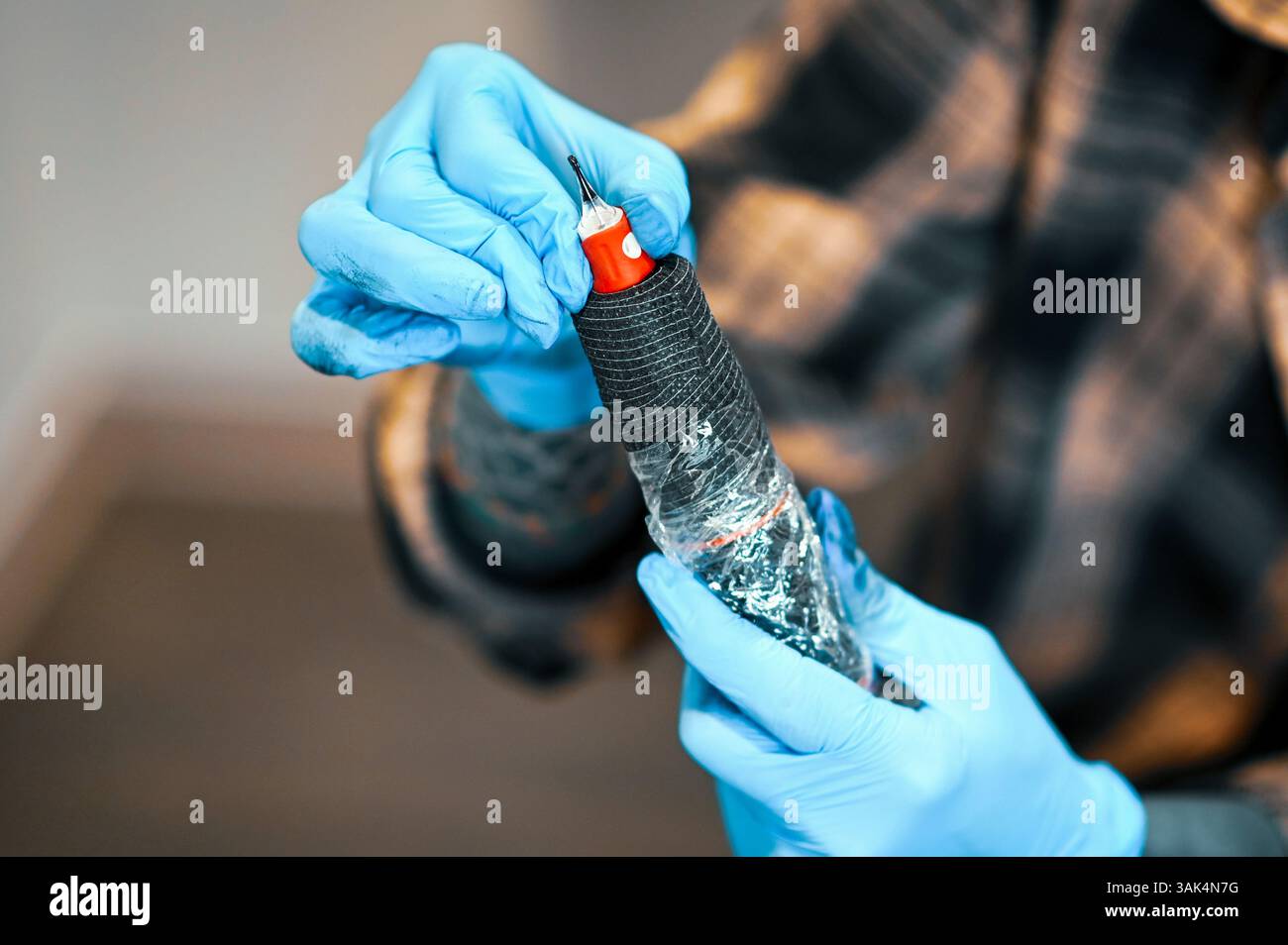 Tätowierer bereitet die Tätowiermaschine vor, wechselt die Nadeln, trägt blaue Handschuhe, Körperkunst und Design Stockfoto