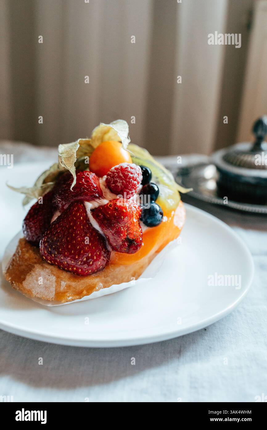 Ein farbenfrohes Obstdessert mit Erdbeeren, Heidelbeeren und anderen Früchten wird auf einem weißen Teller serviert. Das Dessert wird auf einem Tisch mit weichem Stockfoto