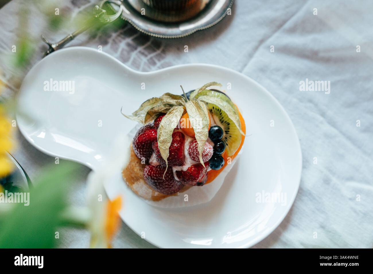 Ein lebendiges Dessert wird auf einem einzigartigen Teller mit Schichten aus Erdbeeren, Heidelbeeren, Kiwi und tropischen Früchten präsentiert. Der Nachtisch ist umgeben Stockfoto