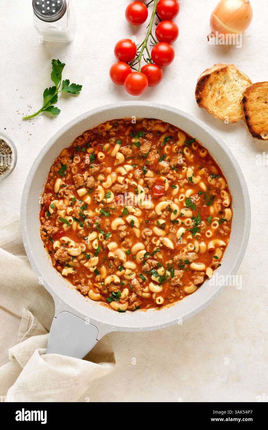 Eine Topfmahlzeit mit Hackfleisch, Pasta und Gemüse in Tomatensoße in einer Pfanne auf hellem Steinhintergrund gekocht. Draufsicht, flach Stockfoto