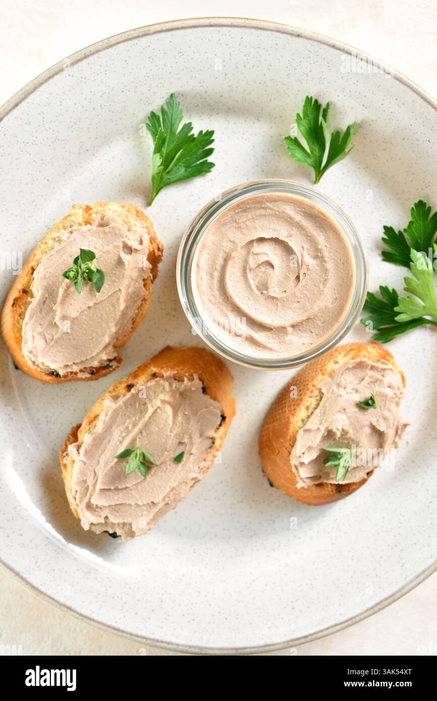 Nahaufnahme der Hühnerleberpastete auf geröstetem Brot auf Teller über hellem Hintergrund. Draufsicht, flach Stockfoto