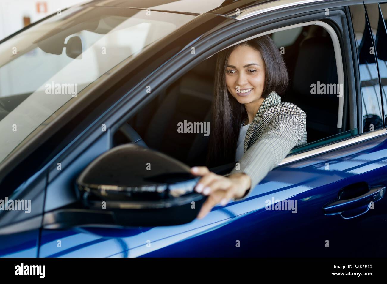 Millennial Frau, die den Seitenspiegel verstellt, während sie im Verkaufsraum des Händlerbetriebs im Fahrzeug sitzt Stockfoto