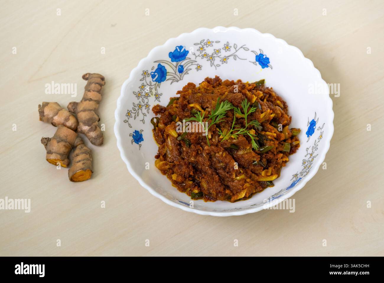 Rohe Kurkuma-Braten oder kacha holud Bhaji, serviert in einer weißen Schüssel auf hellem Holzhintergrund. Es ist ein sehr gesundes und leckeres Essen. Stockfoto