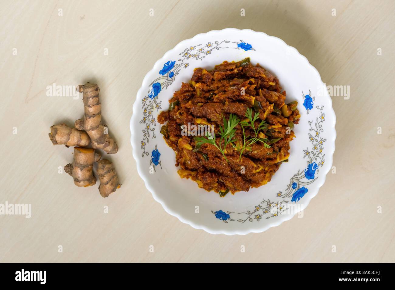Kacha Holud Bhaji (roher Kurkuma-Braten) serviert in einer weißen Schüssel auf hellem Holzhintergrund. Dies ist ein sehr gesundes und leckeres Essen. Draufsicht. Stockfoto
