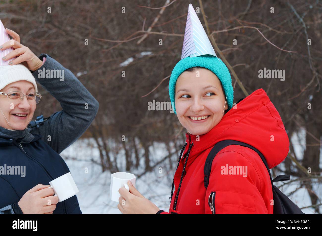 Zwei Freunde genießen im schneebedeckten Wald winterliche Leckereien und feiern mit festlichen Partyhüten Stockfoto