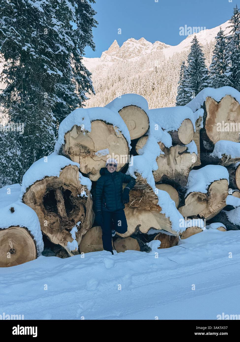 Der Wanderer macht eine Pause und lehnt sich auf einen Stapel schneebedeckter Baumstämme in einem Wintergebirge Stockfoto