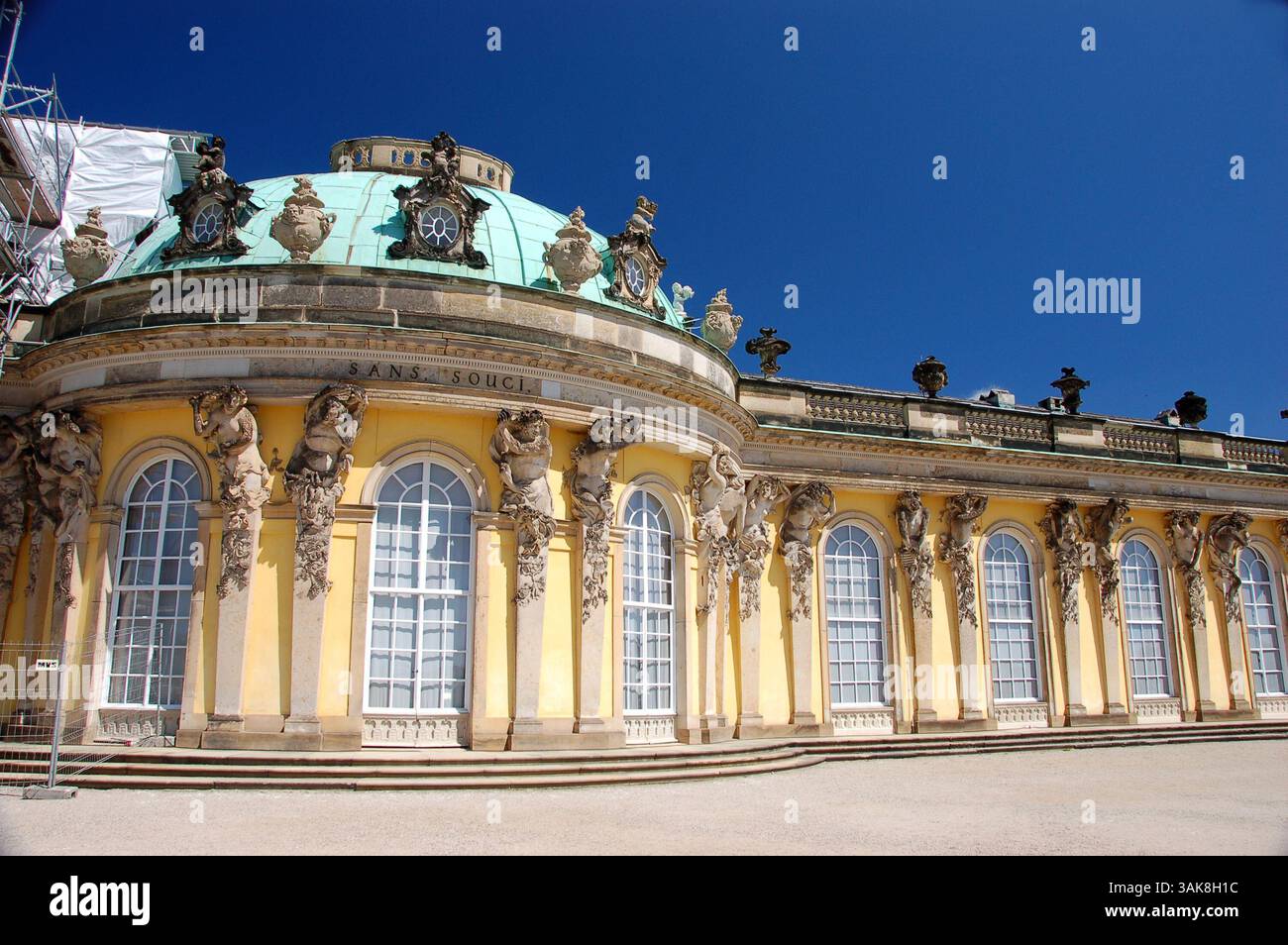 Schloss Sanssouci in Potsdam, Deutschland, mit hellgelber Fassade und kunstvollen Skulpturen unter tiefblauem Himmel Stockfoto