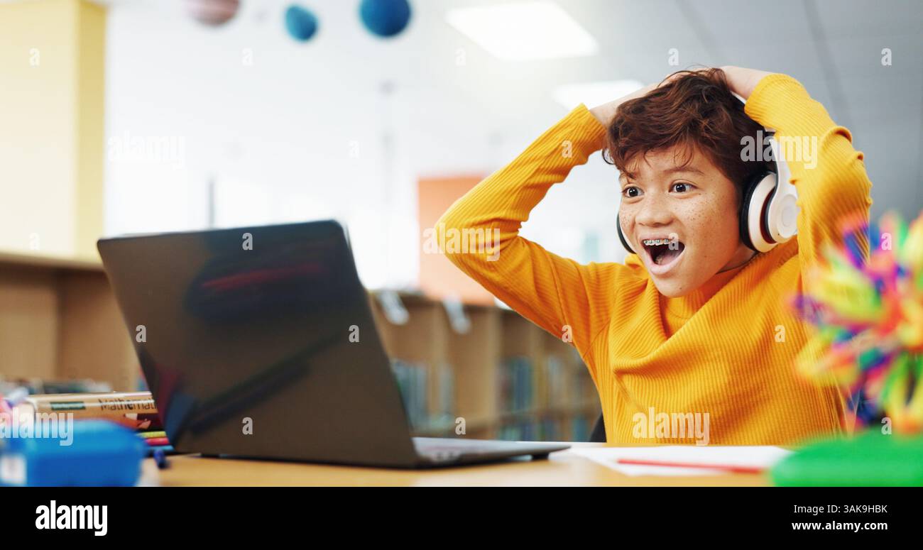 Glückliches Kind, Schüler oder gute Nachrichten mit Laptop für Sieg, elearning oder Notenergebnisse in der Bibliothek. Junge, Kind oder begeisterte Lernende mit Wow, Kopfhörern oder Stockfoto