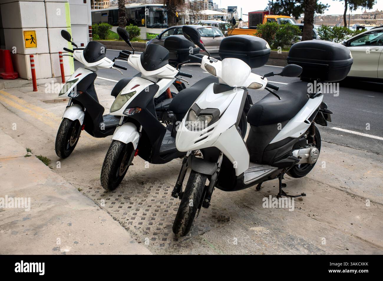 Drei weiße Mietroller mit Top Boxen, die am Straßenrand in einer Küstenstadt geparkt sind. Umweltfreundliche und flexible Transportmöglichkeit für Touristen, die die Stadt erkunden Stockfoto