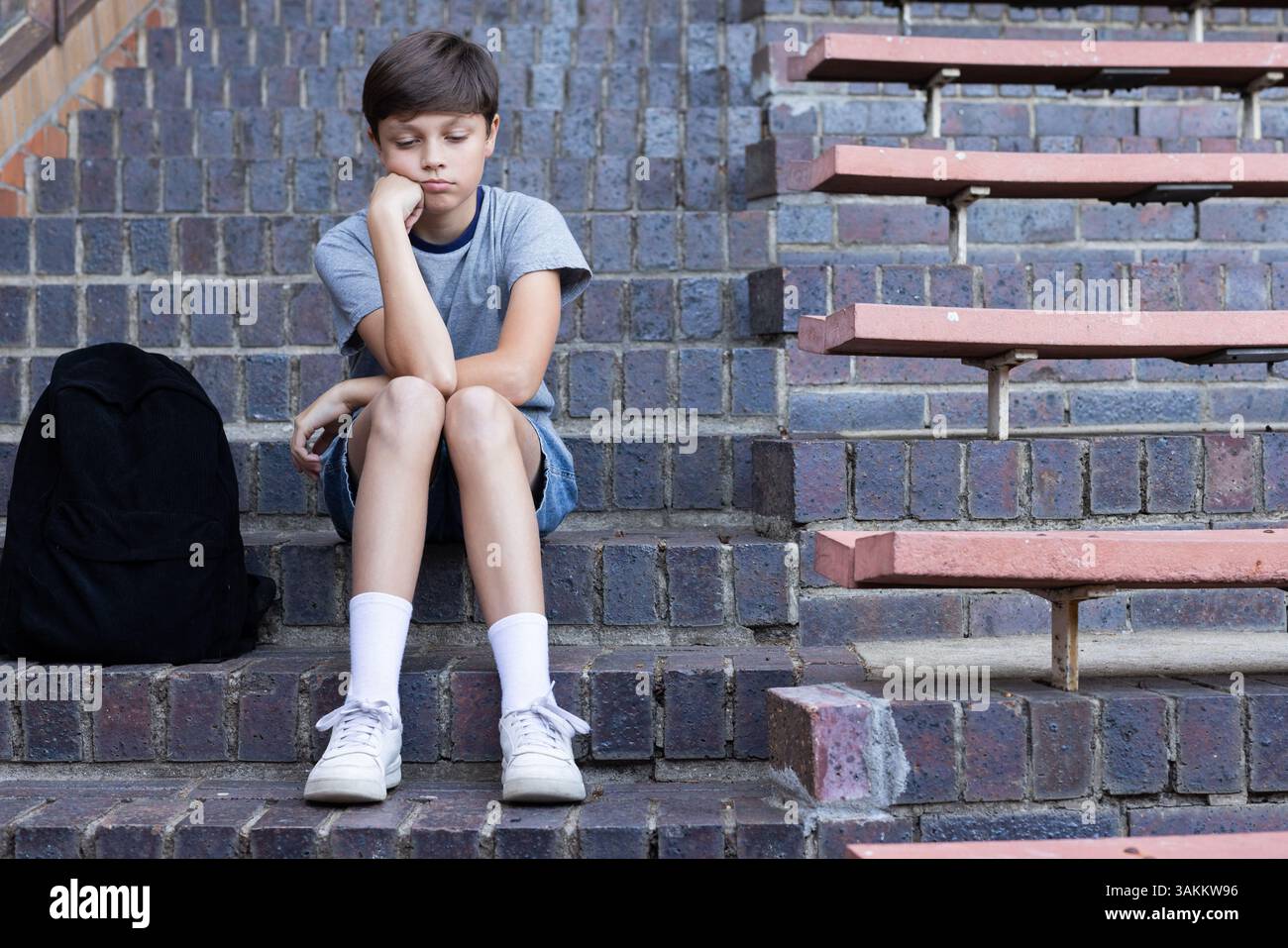 Auf Stufen sitzend, ein Junge, der traurig mit dem Rucksack in der Schule aussieht, Kopierraum Stockfoto