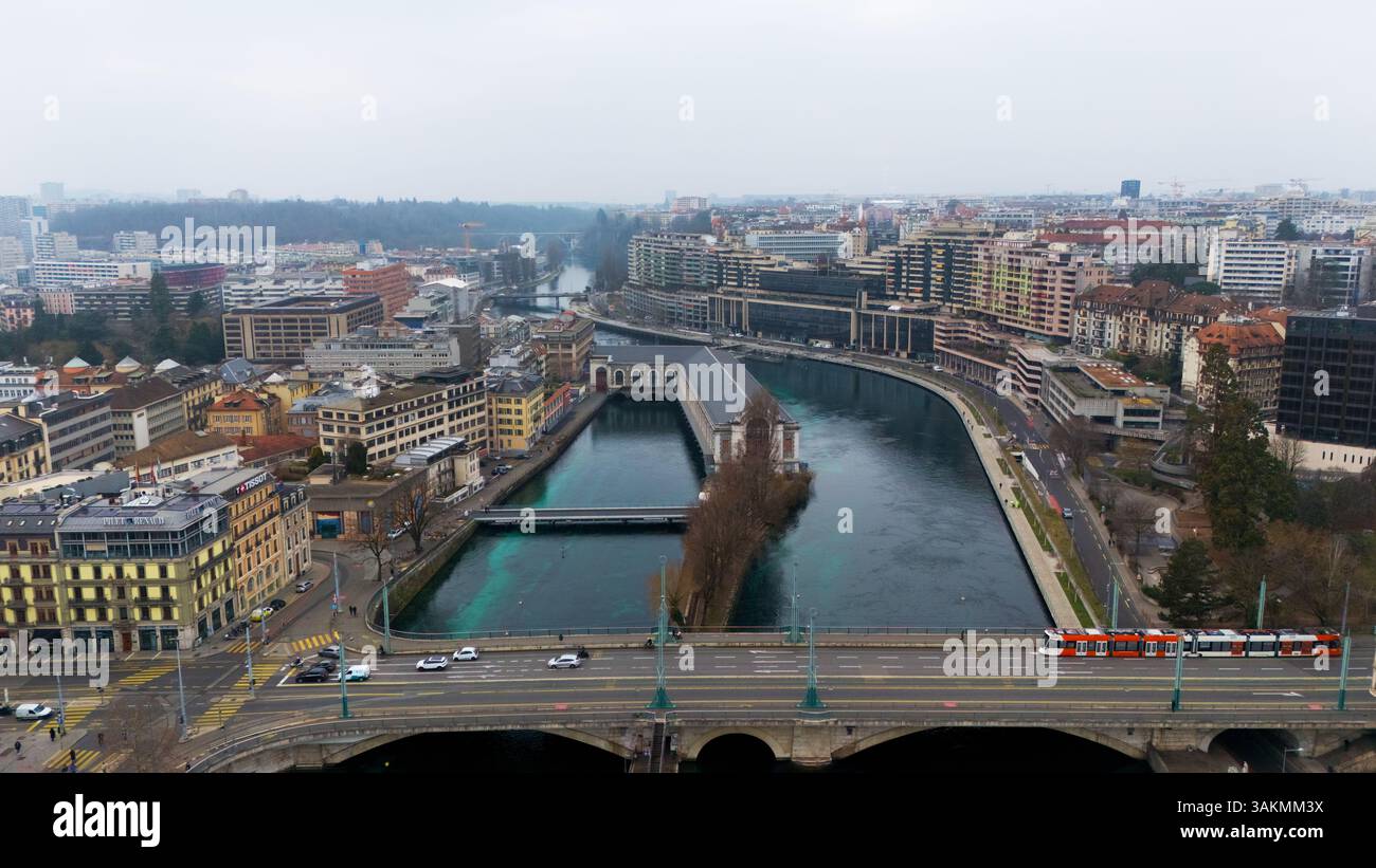 Blick auf die Genfer Drohne auf eine europäische Stadt mit einer Straßenbahn über eine Brücke, farbenfrohen Gebäuden und dem historischen Batiment des Forces Motrices am Fluss. Stockfoto
