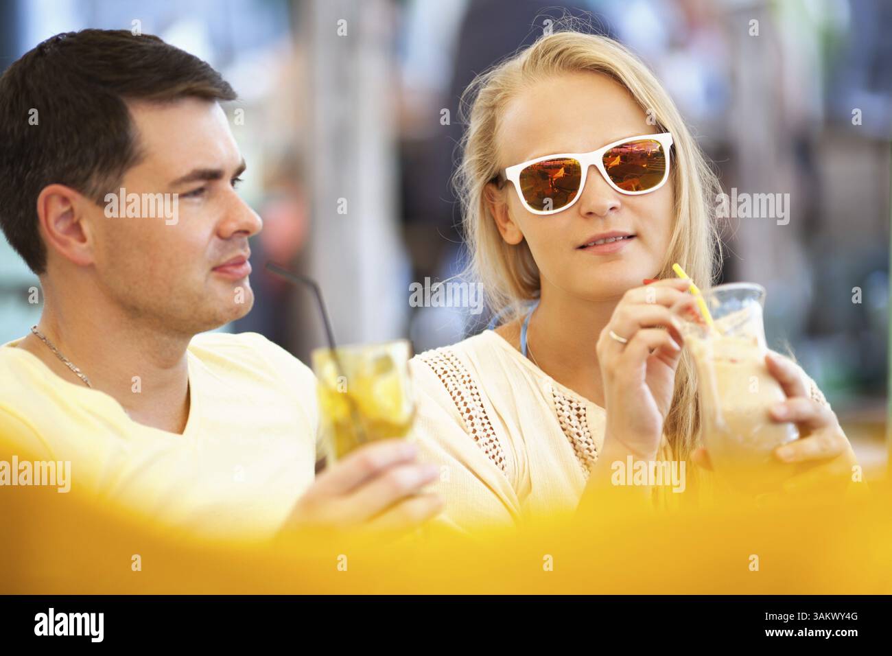 Junges Paar, das sich mit erfrischenden Getränken in langen Gläsern im Sommerurlaub entspannt und sich auf eine attraktive Frau mit Sonnenbrille konzentriert Stockfoto