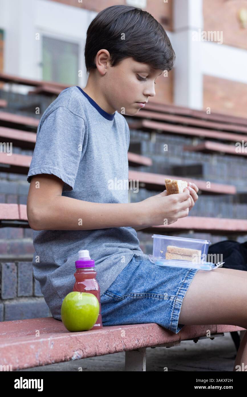Während der Mittagspause in der Schule isst man Sandwiches, der Junge sitzt auf einer Treppe im Freien Stockfoto