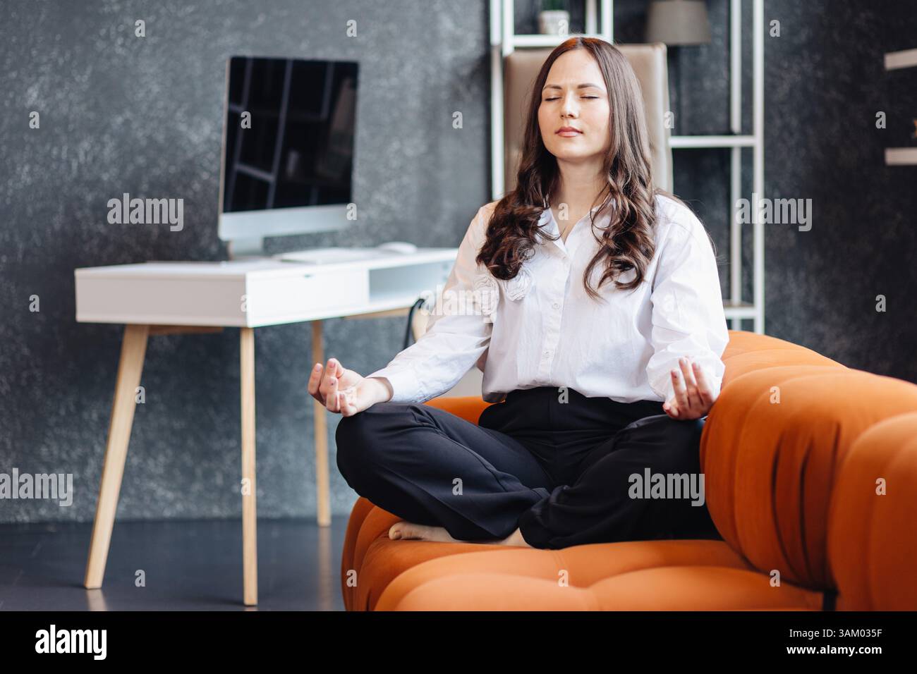 Eine Frau, die in Lotusposition während einer Pause im Büro meditiert, um Entspannung und Achtsamkeit im beruflichen Umfeld zu fördern. Stockfoto