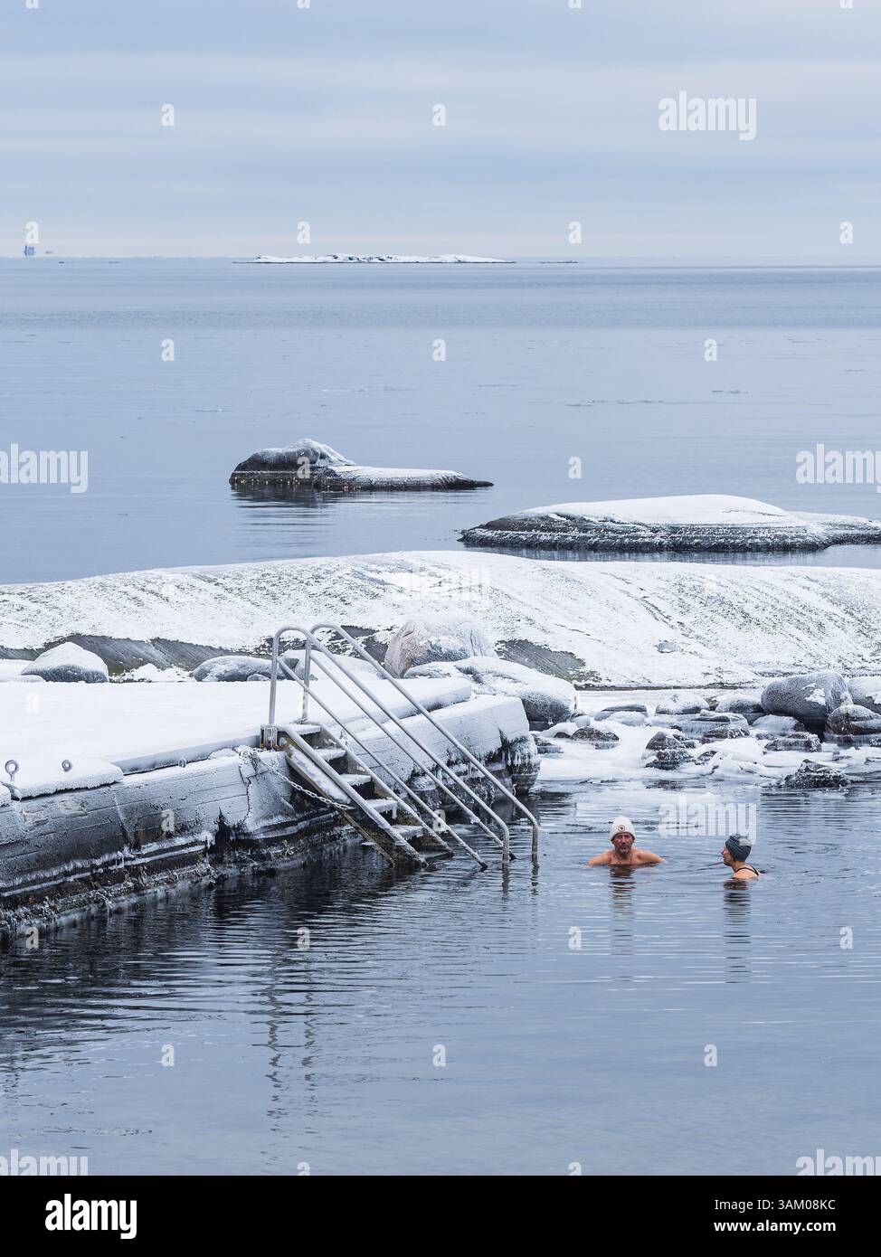 Zwei Personen nehmen ein erfrischendes Winterbad im ruhigen, kalten Wasser entlang der malerischen Küste außerhalb von Göteborg, umgeben von Schnee Stockfoto