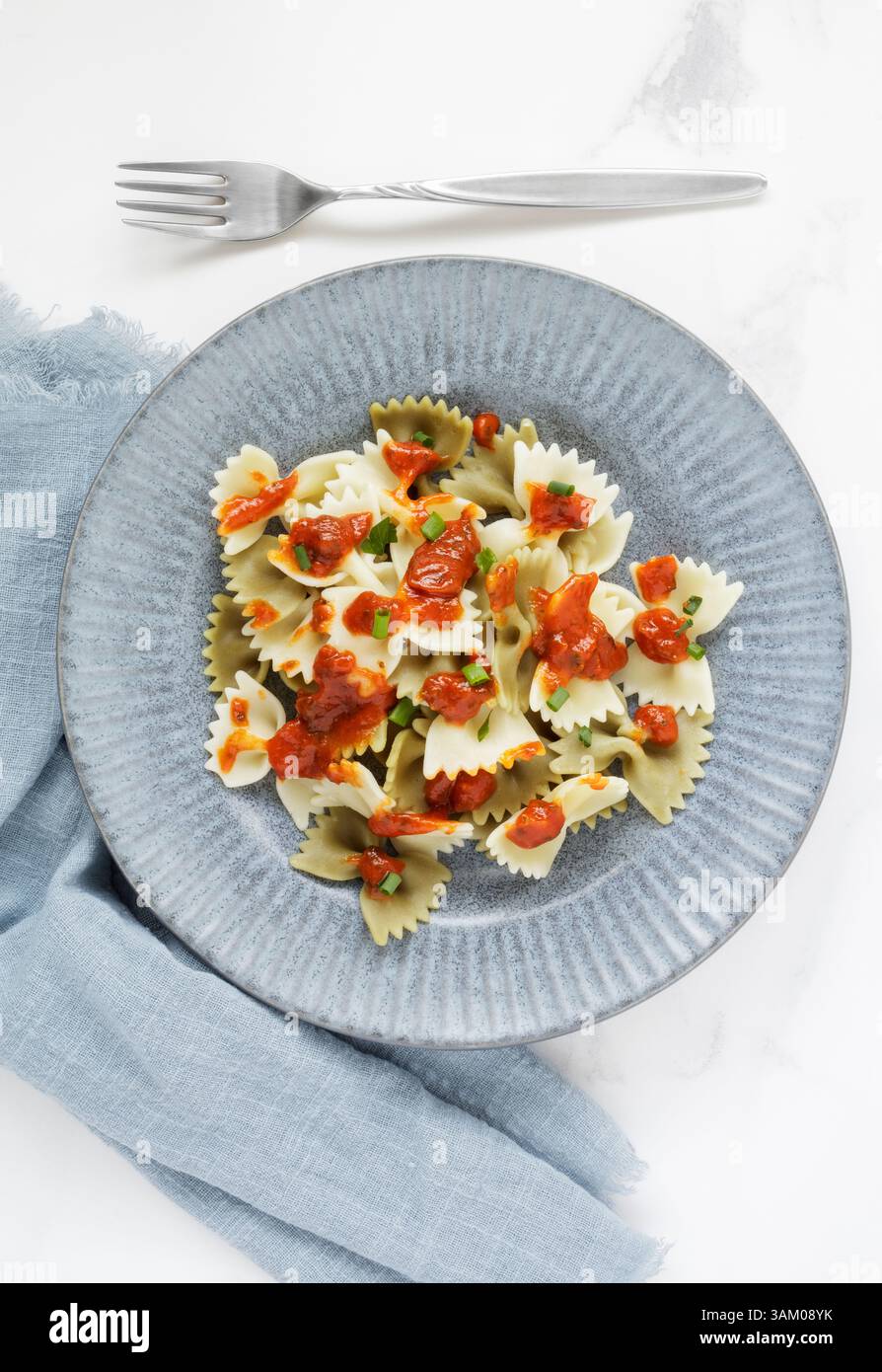 Ein Teller gekochte Farfalle-Pasta mit Tomatensoße garniert mit frischen Kräutern Stockfoto