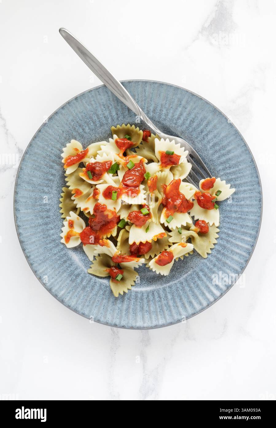 Ein Teller mit gekochter Farfalle-Pasta mit Tomatensauce auf weißem Marmortisch Stockfoto