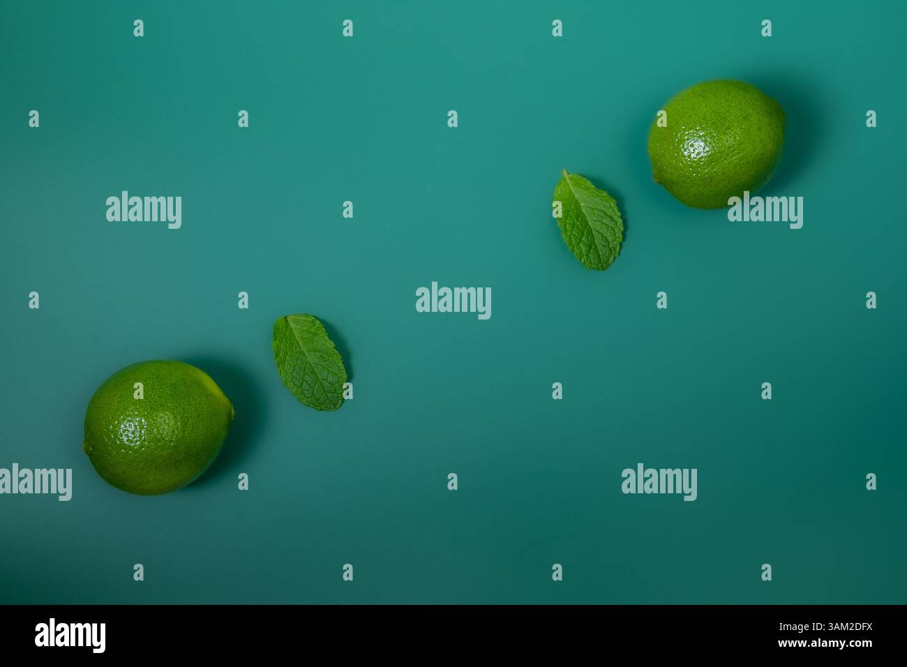 Limes and Mint Leaves diagonal auf grünem Hintergrund angeordnet – Draufsicht Stockfoto