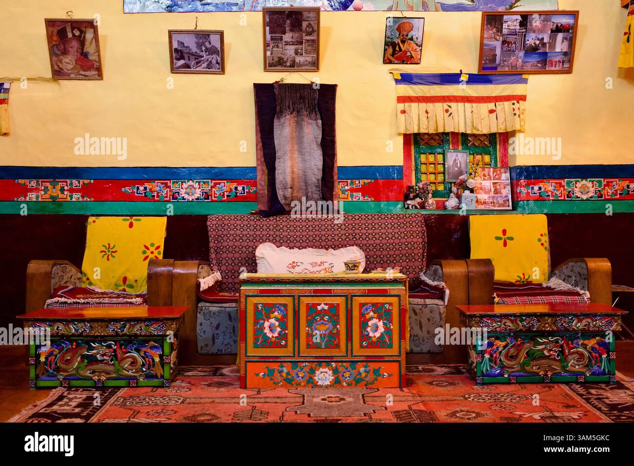 Empfangsraum im Stakna Kloster in Ladakh, mit bemalten Möbeln, Wandbehängen und gerahmten Fotos von religiösen Figuren und klösterlichem Leben. Stockfoto