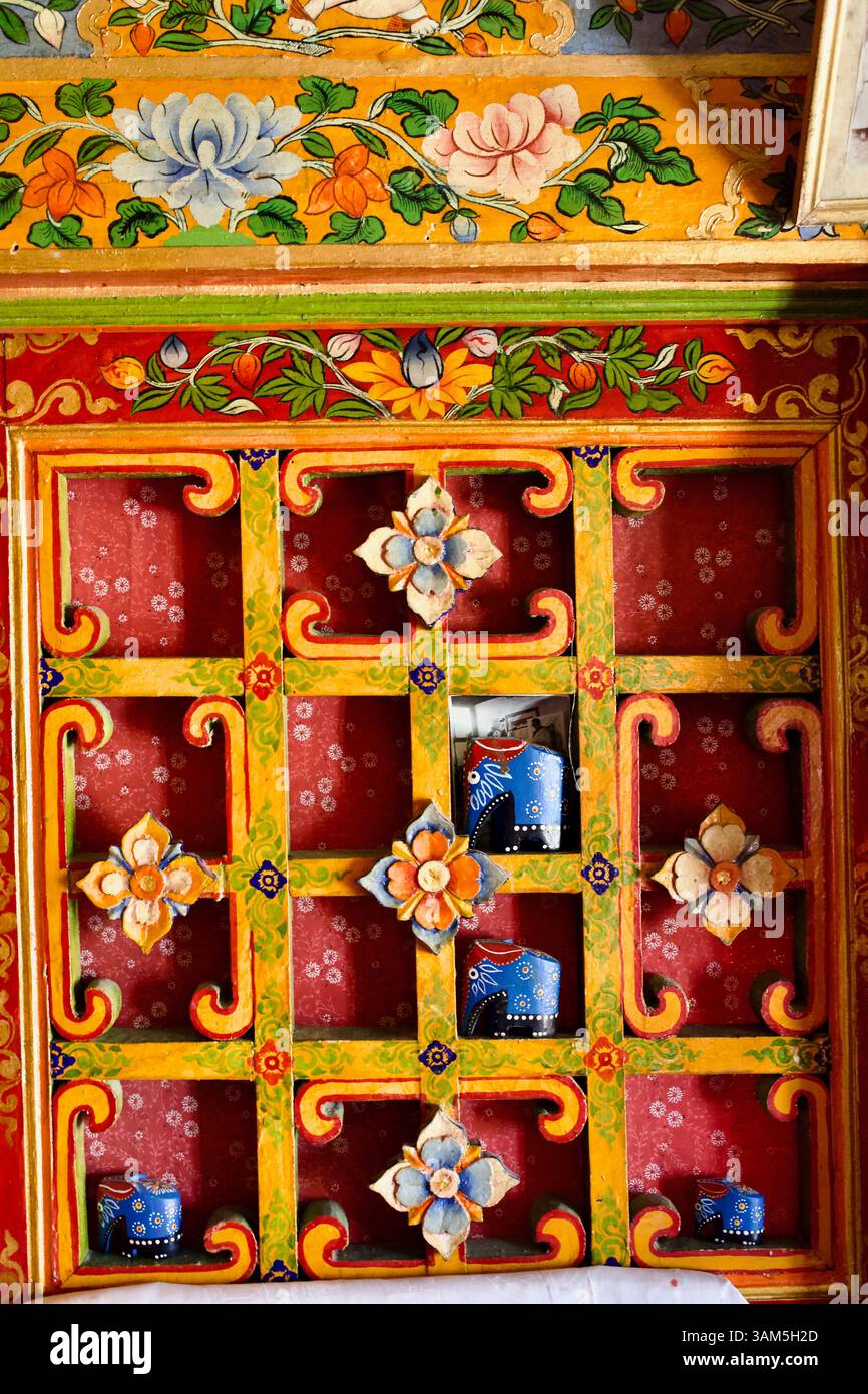 Detail eines bemalten Holzkabinetts im Kloster Stakna, Ladakh, mit Blumenmotiven und Votivopfergefäßen hinter Gittern. Stockfoto