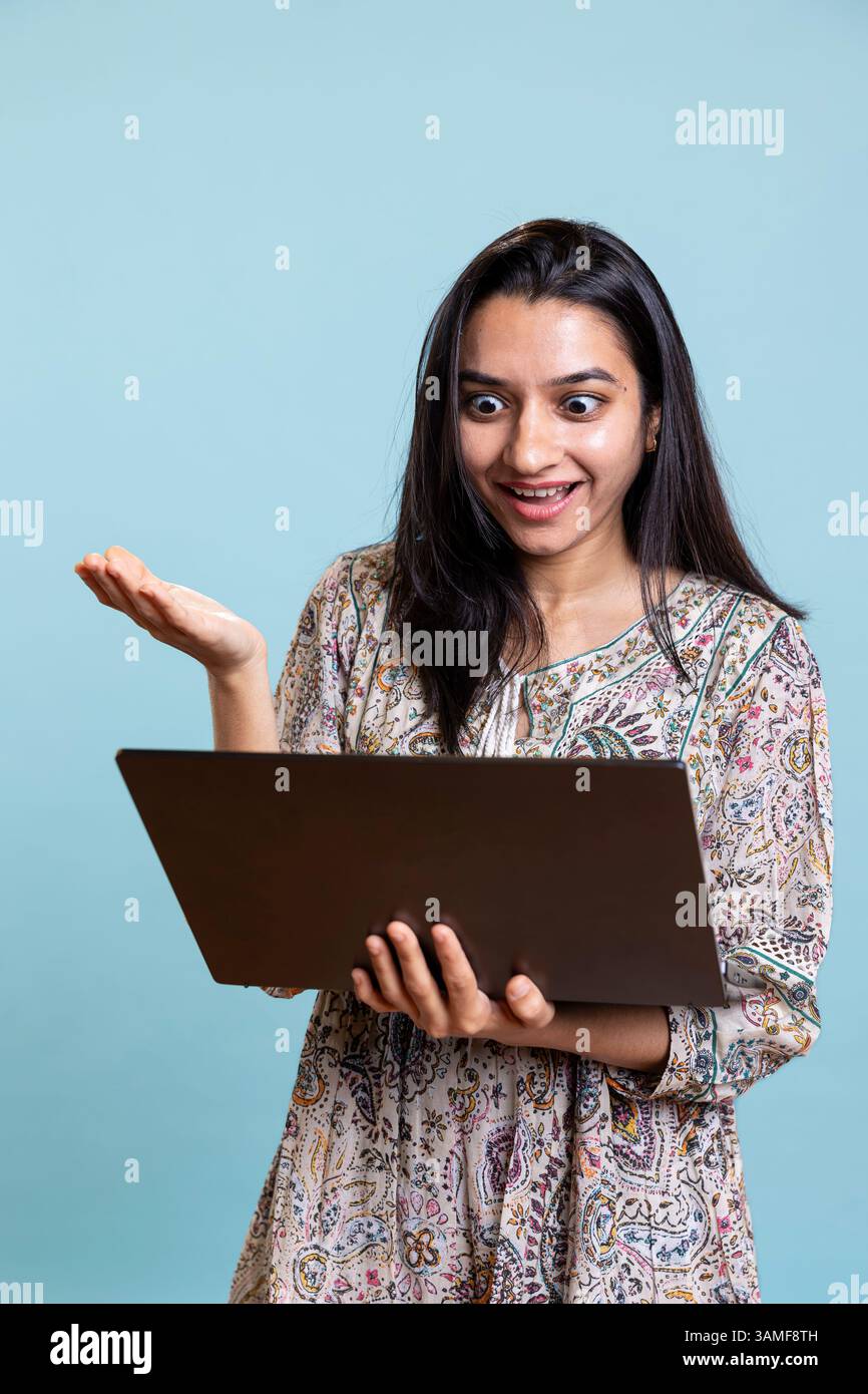 Fröhliche Person, die mit Freunden bei einer Videokonferenz tratscht, posiert vor dem Hintergrund des Studios. Glückliche, entspannte Frau, die sich mit ihren Mädchen verbündet, nehmen Sie an Online-Videogesprächen auf dem Laptop Teil. Stockfoto