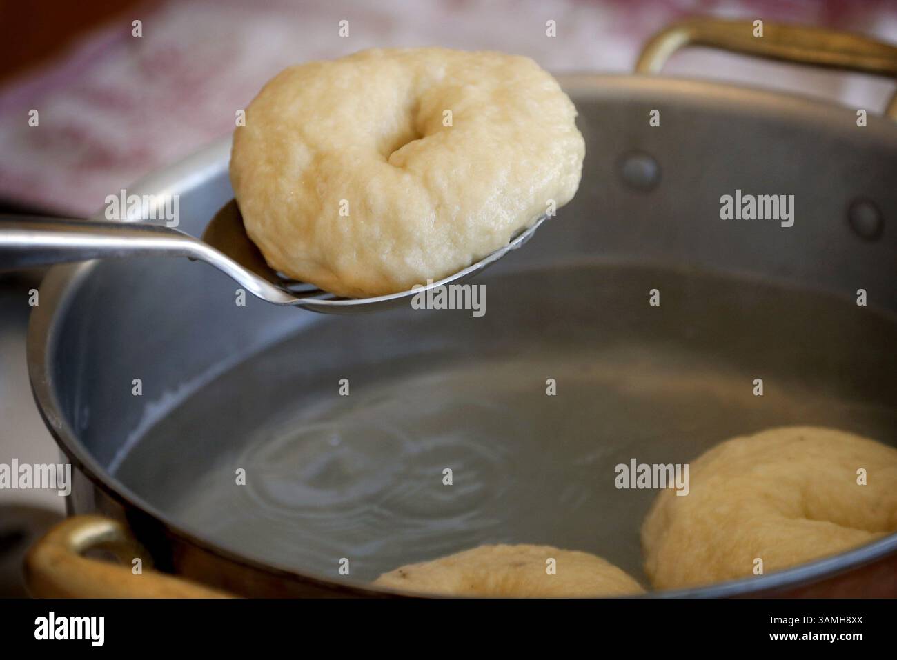 Jan. 2014 – Edina, MN, USA – senken Sie die drei Bagels vorsichtig mit der Oberseite nach unten in das kochende Wasser, sodass sie genügend Platz zum Schwimmen haben. (Sie sinken zuerst und steigen dann auf.) Pochiere eine Minute, dann drehe sie um und lasse sie noch eine Minute pochieren. Die Bagels mit einem Löffel entfernen und auf ein vorbereitetes Backblech legen. Wiederholen Sie den Vorgang mit 3 weiteren Bagels. (Kreditbild: © Carlos Gonzalez/MCT/ZUMAPRESS.com) Stockfoto