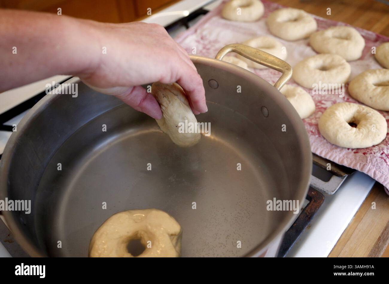 Jan. 2014 – Edina, MN, USA – senken Sie die drei Bagels vorsichtig mit der Oberseite nach unten in das kochende Wasser, sodass sie genügend Platz zum Schwimmen haben. (Sie sinken zuerst und steigen dann auf.) Pochiere eine Minute, dann drehe sie um und lasse sie noch eine Minute pochieren. Die Bagels mit einem Löffel entfernen und auf ein vorbereitetes Backblech legen. Wiederholen Sie den Vorgang mit 3 weiteren Bagels. (Kreditbild: © Carlos Gonzalez/MCT/ZUMAPRESS.com) Stockfoto