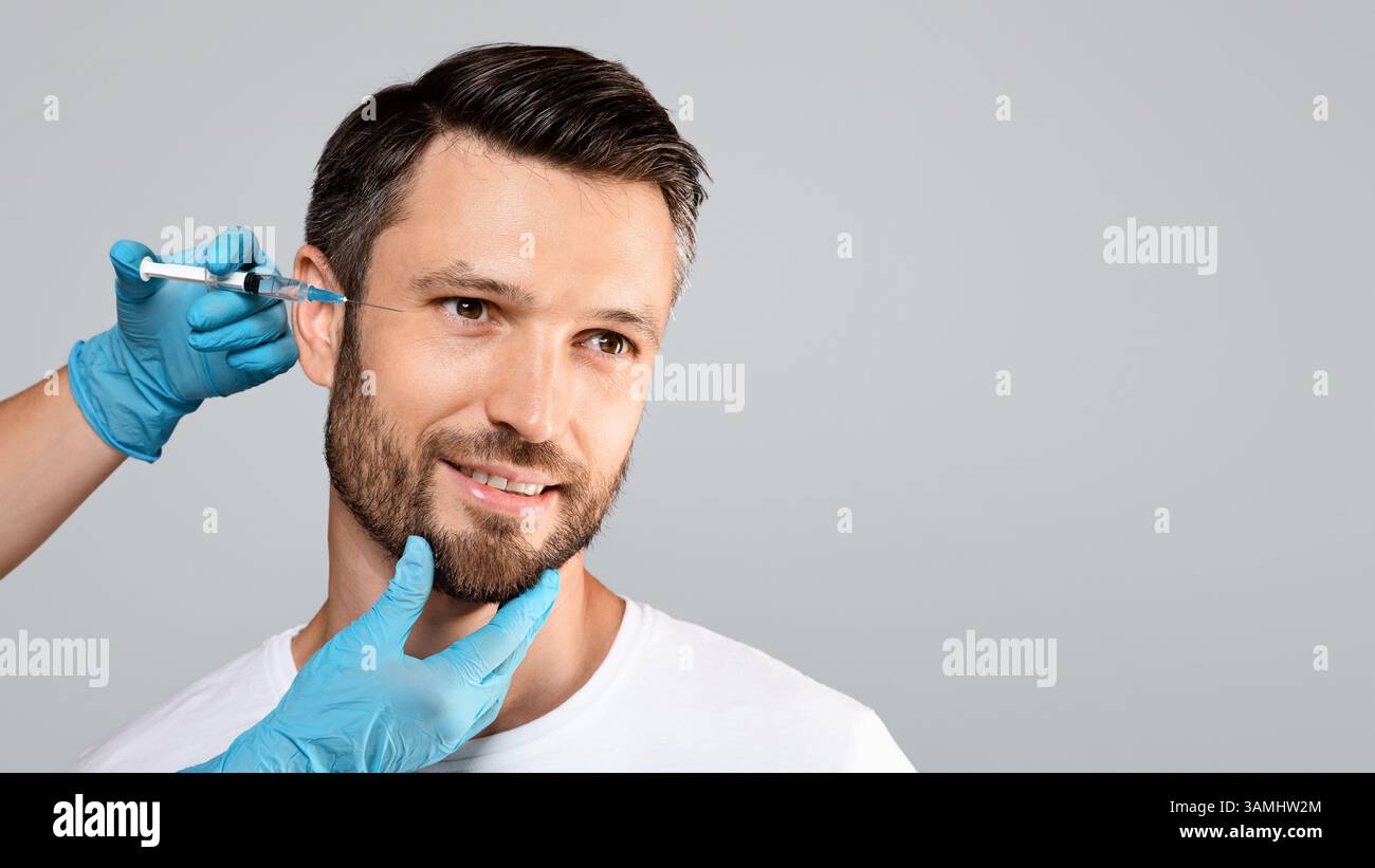 Hübscher Mann, der unter Augeninjektionen kommt, grauer Hintergrund, leerer Raum Stockfoto