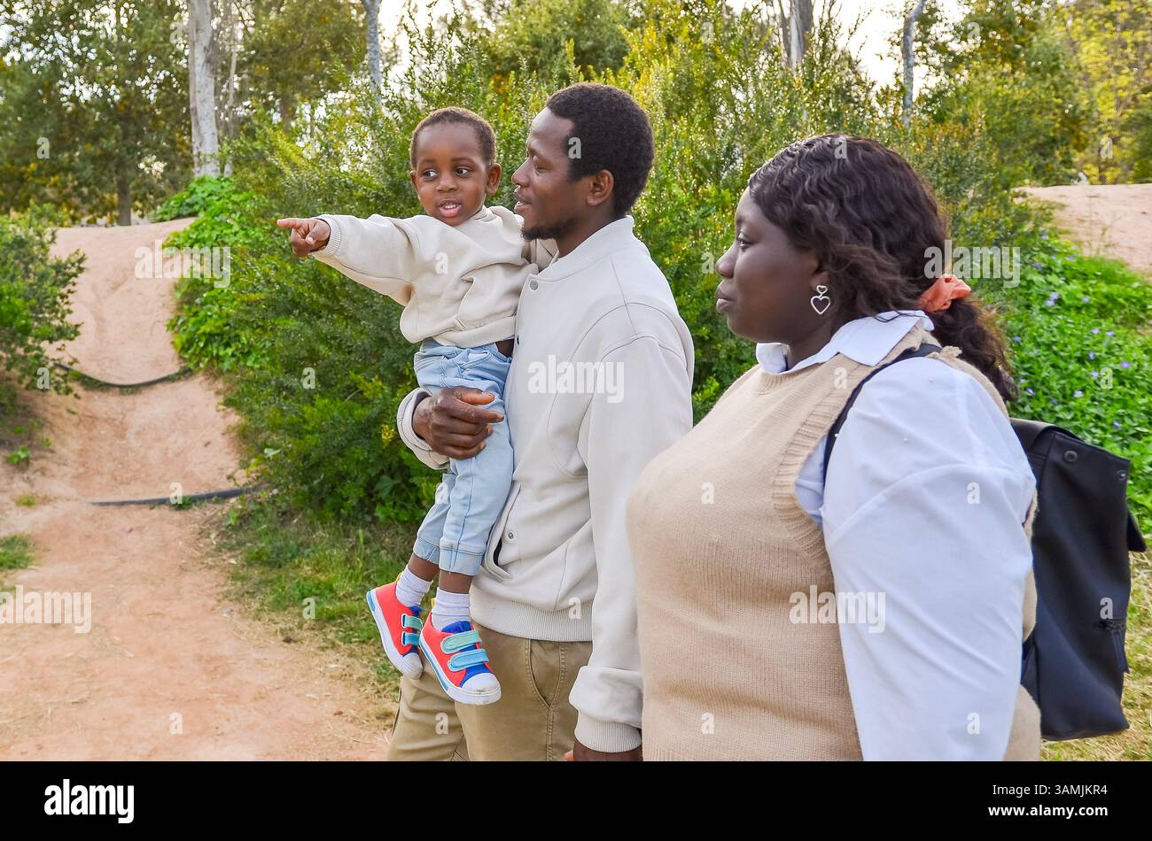 Lächelnde afroamerikanische Familie macht einen Spaziergang im Park, während ihr Kind auf etwas in der Ferne zeigt Stockfoto