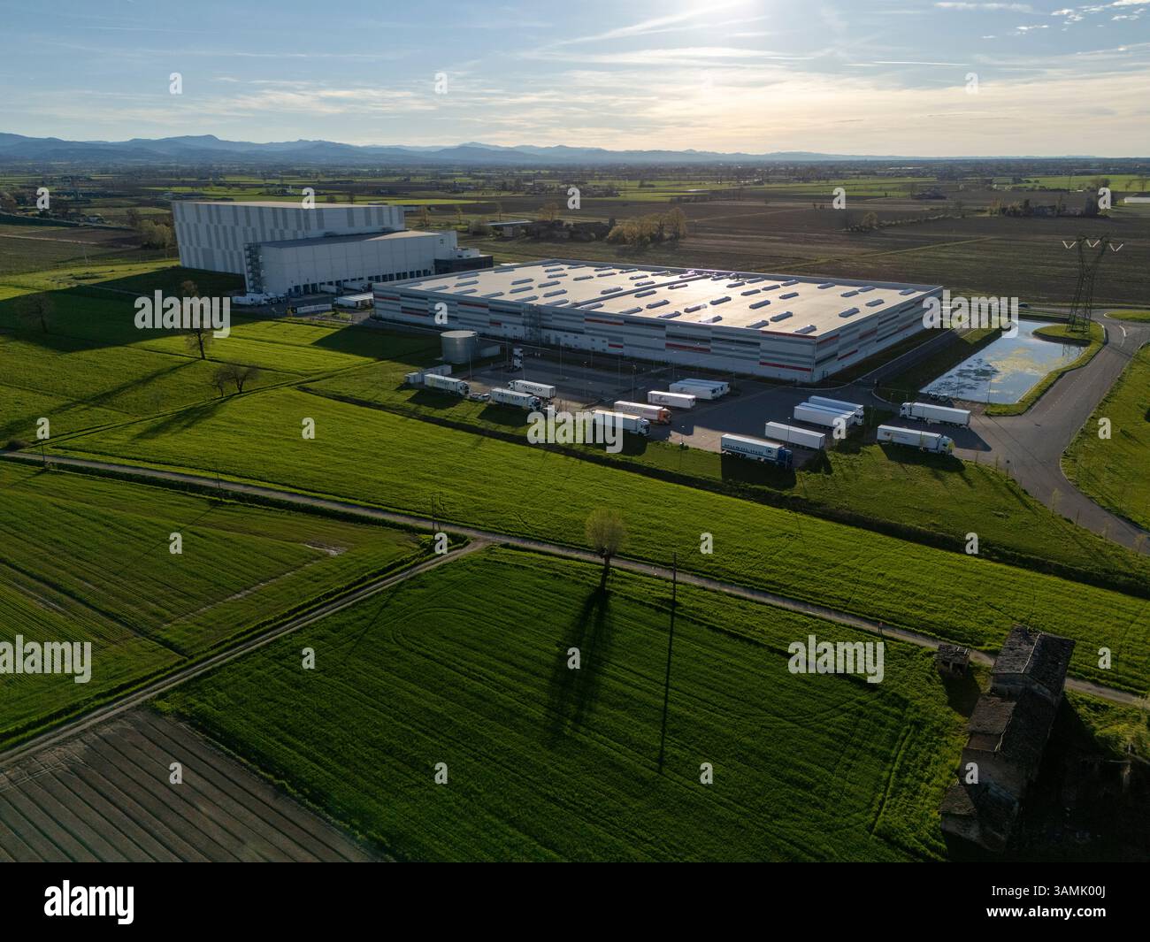 PC, Italien - 26. März 2025 - Luftaufnahme eines 40 Meter hohen automatisierten Kühlhauses in Norditalien, umgeben von grünen Feldern und Park Stockfoto
