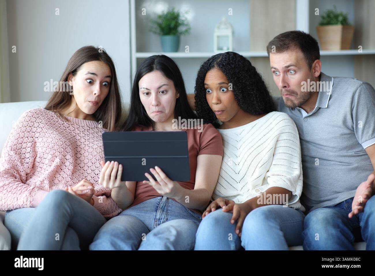 Verwirrte Gruppe von Freunden, die zu Hause auf einer Couch sitzen, um ein Tablet zu überprüfen Stockfoto