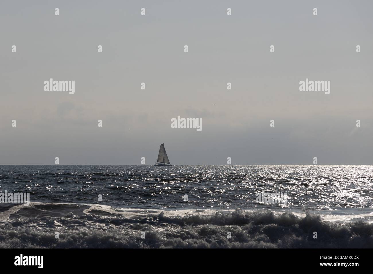 Segelboot am Horizont unter bewölktem Himmel, gleitet bei Sonnenuntergang über glitzernde Meereswellen. Friedliche Meereslandschaft, perfekt für Reisen Stockfoto