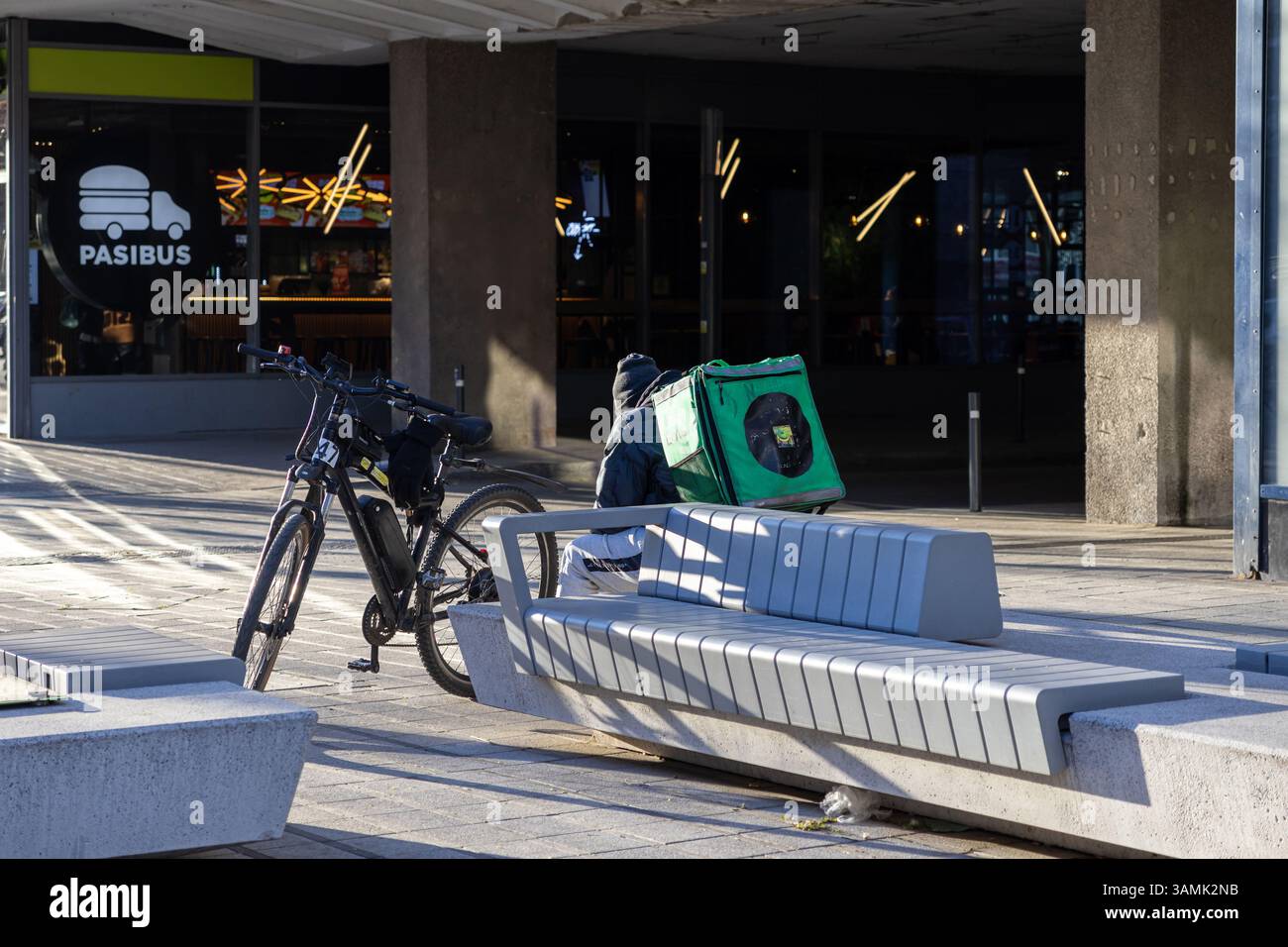 Posen, Polen - 8. April 2025: Fahrradfahrer mit einem grünen isolierten Rucksack machen auf einer Bank vor dem Pasibus Burger Restaurant eine Pause Stockfoto