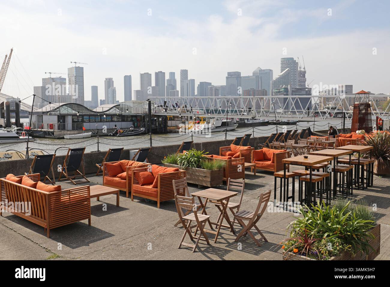 Sitzplätze im Freien an der Trinity Buoy Wharf in den Londoner docklands, Großbritannien. Zeigt die Canary Wharf Türme dahinter. Stockfoto