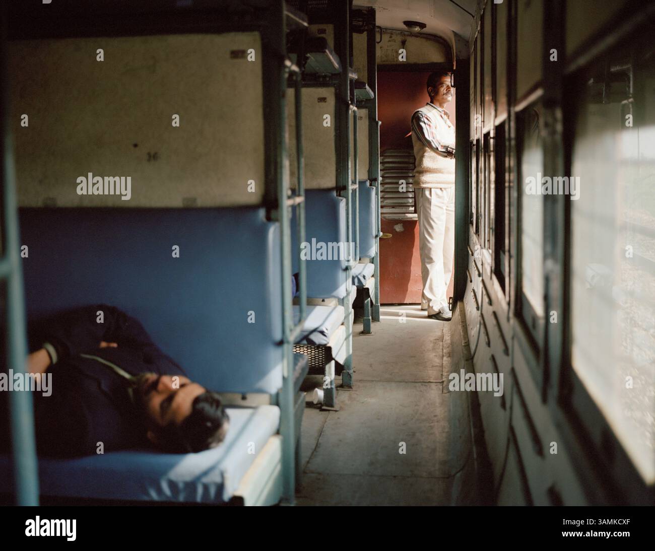Ein Mann fährt mit dem Zug durch Rajastan und beobachtet, wie das Land vorbeizieht, während ein anderer im Januar 2002 auf freiem Platz ein Nickerchen macht Stockfoto