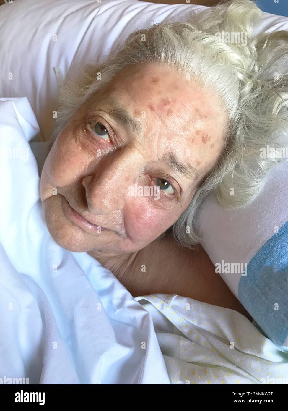 Alte Dame im Bett, lächelt und sieht in die Kamera. Stockfoto