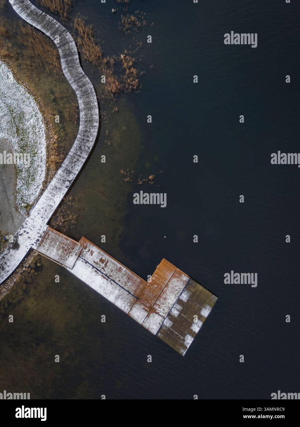 Blick aus der Vogelperspektive auf eine wunderschöne Fußgängerbrücke über einen gefrorenen See, umgeben von einer ruhigen Winterlandschaft, Trakai, Litauen. Stockfoto