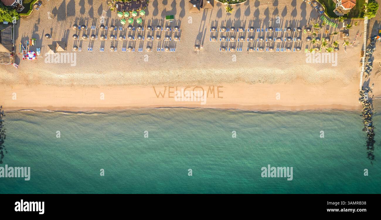 Blick aus der Vogelperspektive auf den Küstenstrand, Sonnenschirme und Willkommensschild in Al Aqah, Dubai. Stockfoto