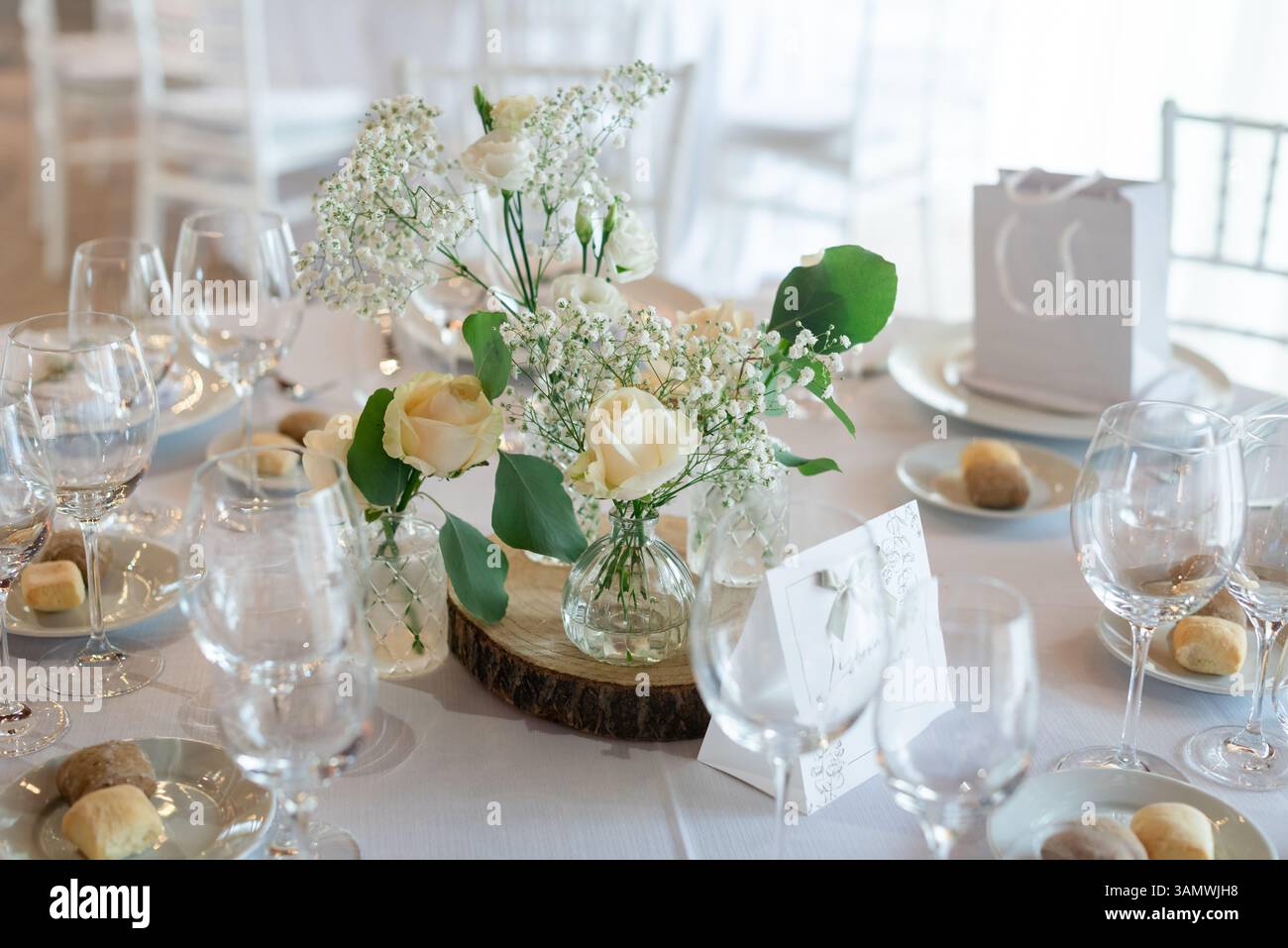 Schöne Anordnung von Rosen und Blumen auf einem Esstisch, umgeben von Glaswaren, schaffen eine romantische Atmosphäre für Gäste. Stockfoto